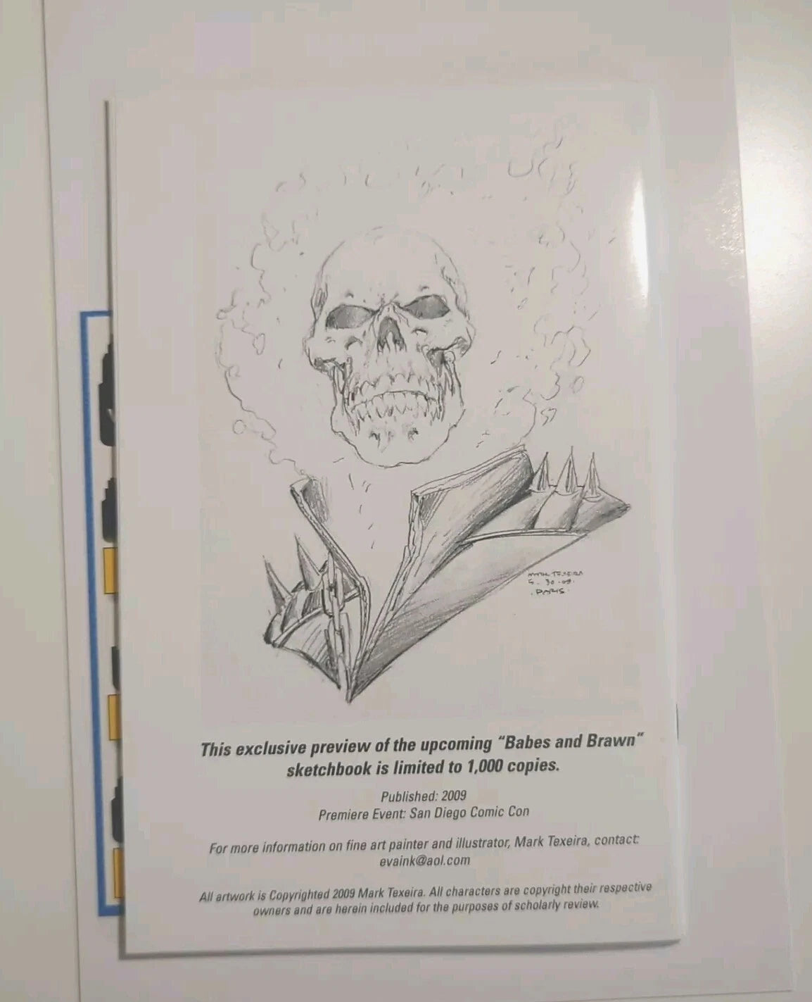 A printed preview sheet for a sketchbook featuring a black-and-white illustrated skull with a folded jacket and several lines of release text below, photographed against a light background.