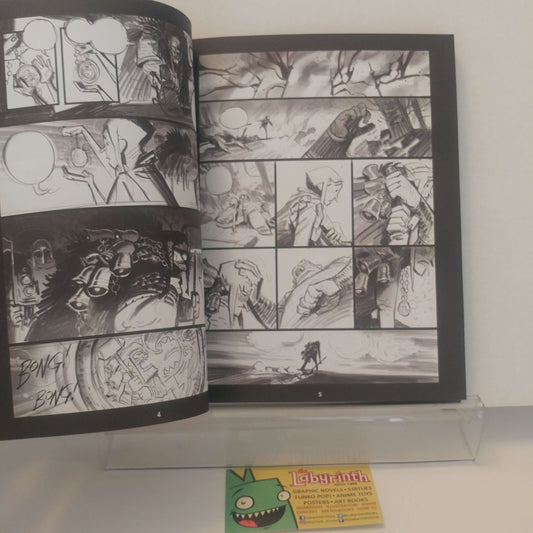 An open black-and-white comic book or art booklet displayed on a clear acrylic stand against a white wall. The pages contain multiple illustrated panels in a monochrome comic-style drawing.