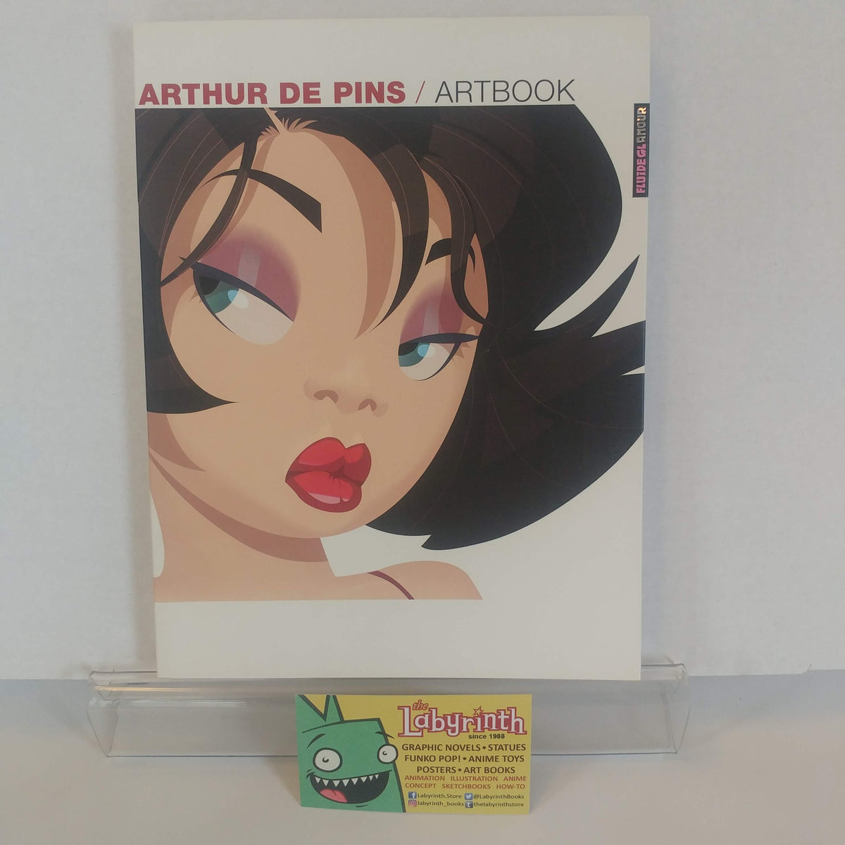 Arthur De Pins Artbook comic book displayed on a clear acrylic stand, with a small Labyrinth trading card in front of it against a plain white background.