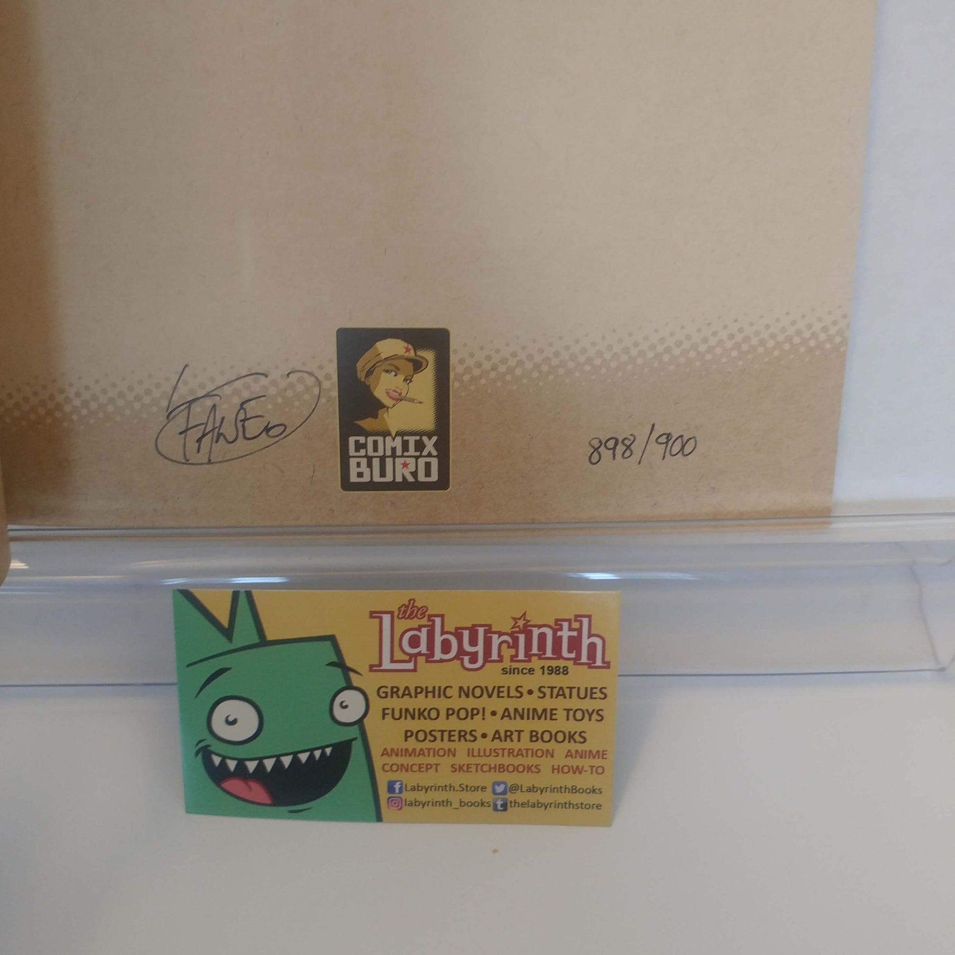 A close-up of a cardboard box with a signed COMIX Buro logo, a handwritten number, and a 'The Labyrinth' character sticker on a white surface.