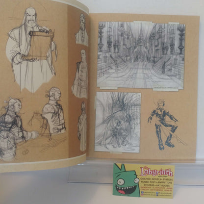 An open sketchbook or art book displaying pencil and ink character and environment drawings on tan paper, with a small Labyrinth toy card visible at the bottom.