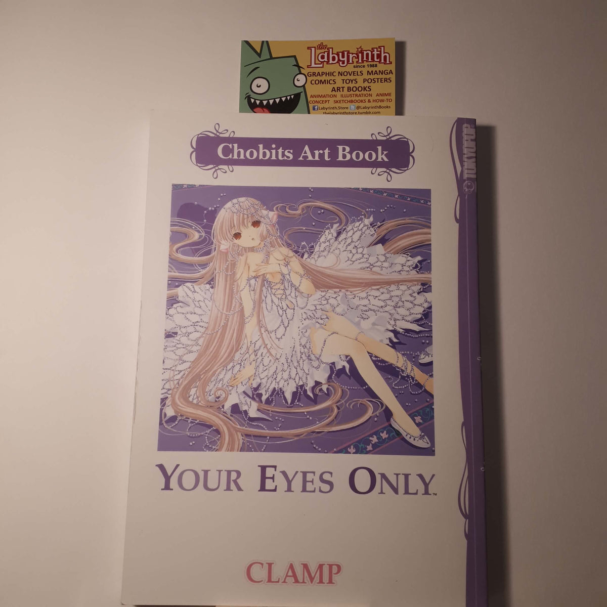 Chobits Art Book 'Your Eyes Only' by Clamp, featuring an anime illustration of a fairy-like character with long pink hair and wings on a purple background. A small card for Labyrinth is placed above the book, and a purple pen is resting on the right side.