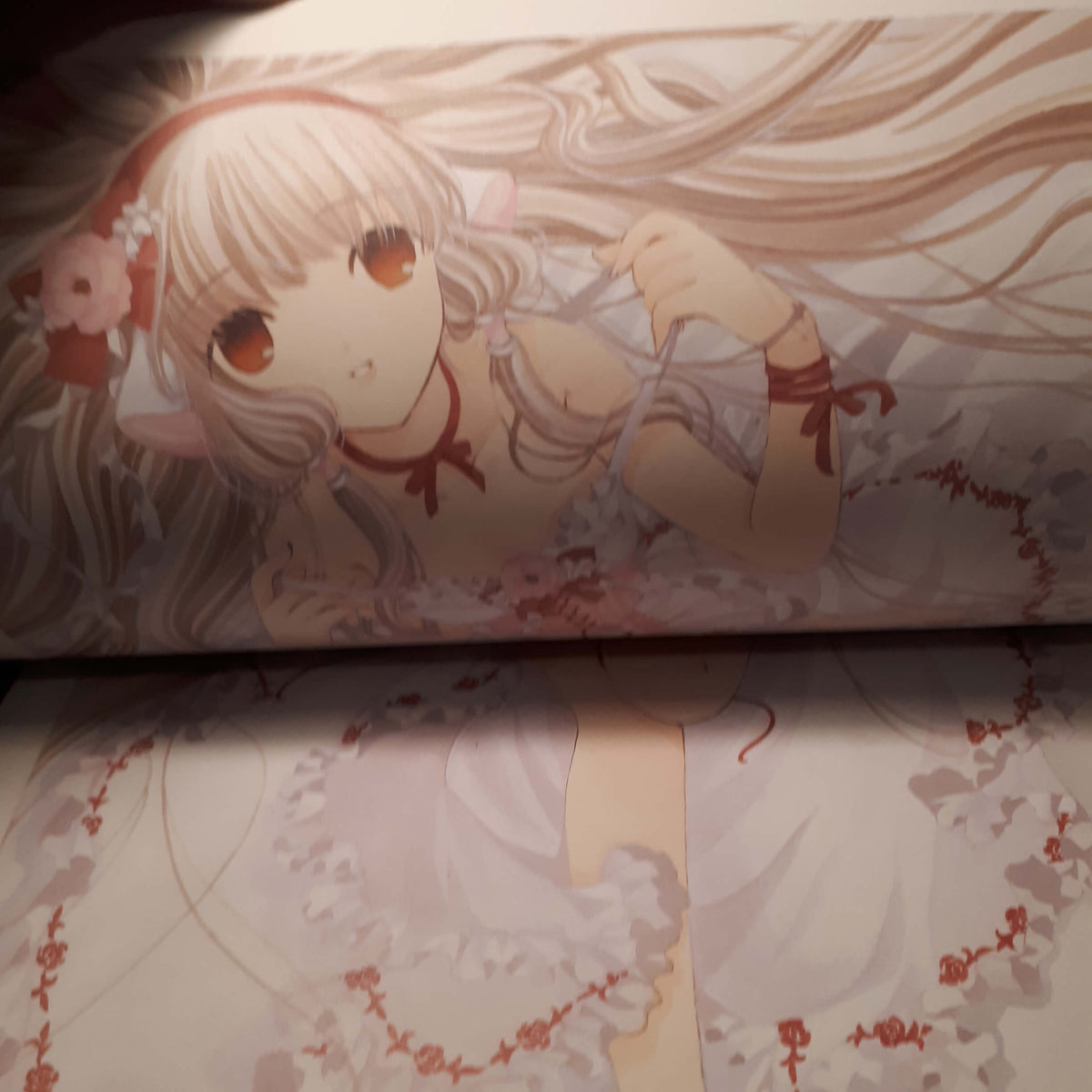 A close-up of printed artwork featuring an anime-style girl with long pale blonde hair, large brown eyes, and a white dress with red ribbon details, shown on a printed surface. from chobits your eyes only artbook