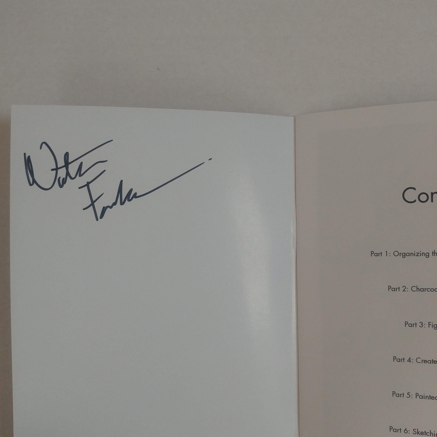 An open book or booklet showing a white signature page with a dark ink signature on the left page and a light beige instruction or table of contents page on the right page.