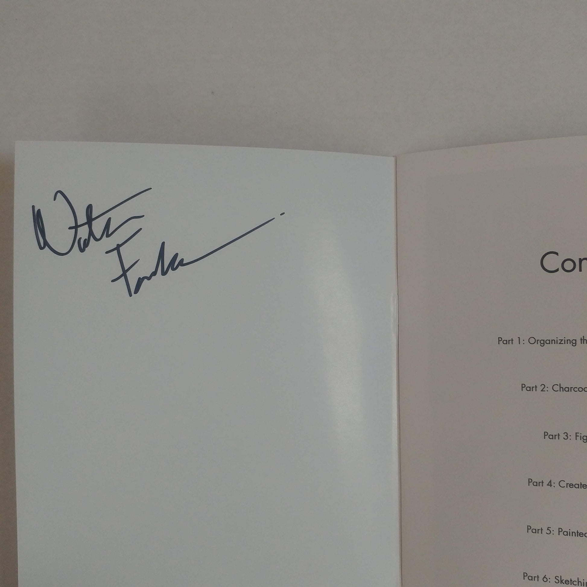 An open book or booklet showing a white signature page with a dark ink signature on the left page and a light beige instruction or table of contents page on the right page.