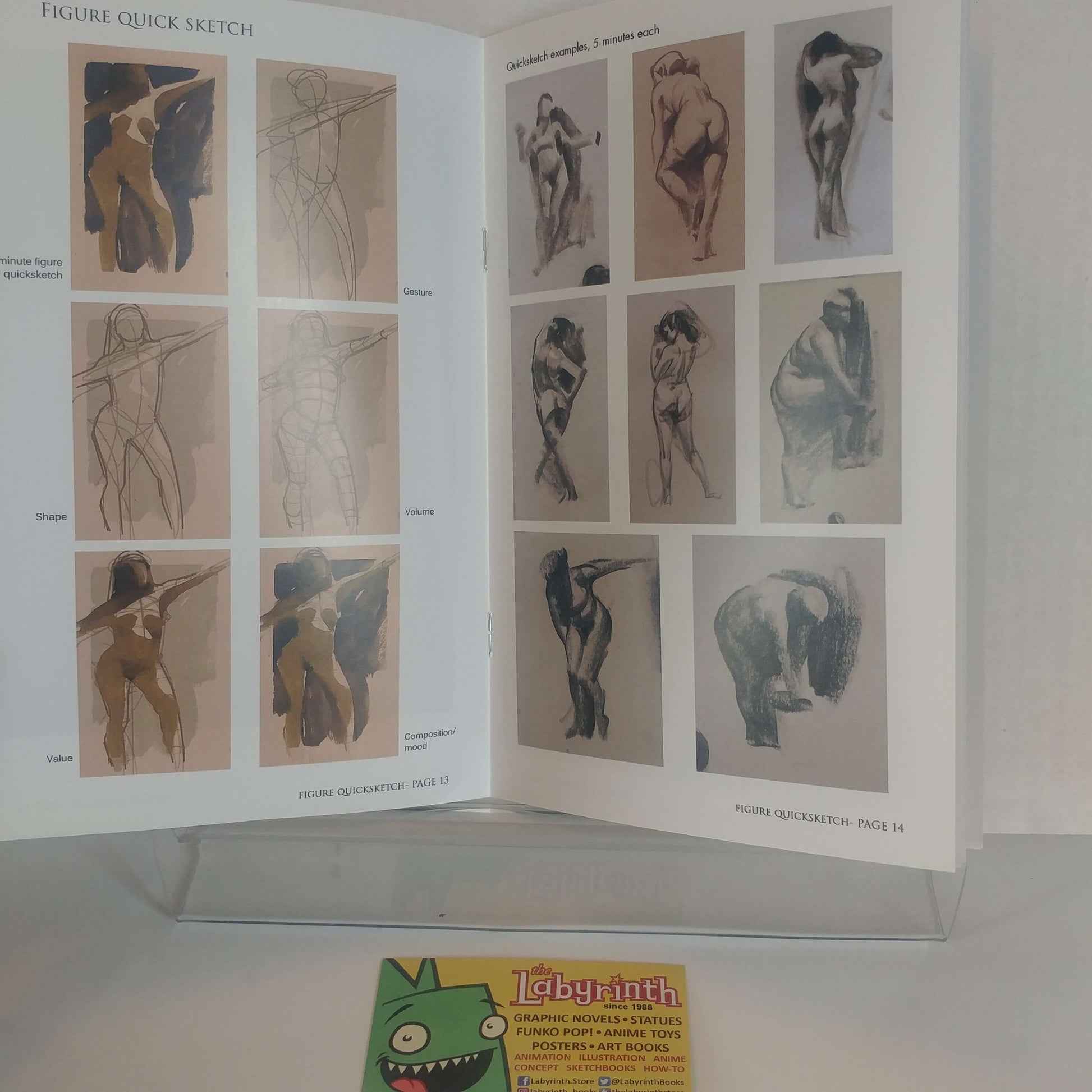 An open art sketch book or instruction booklet displayed on a clear acrylic stand, showing multiple figure drawing pages. A small green cartoon card with the word 'Labyrinth' is visible in front at the bottom.