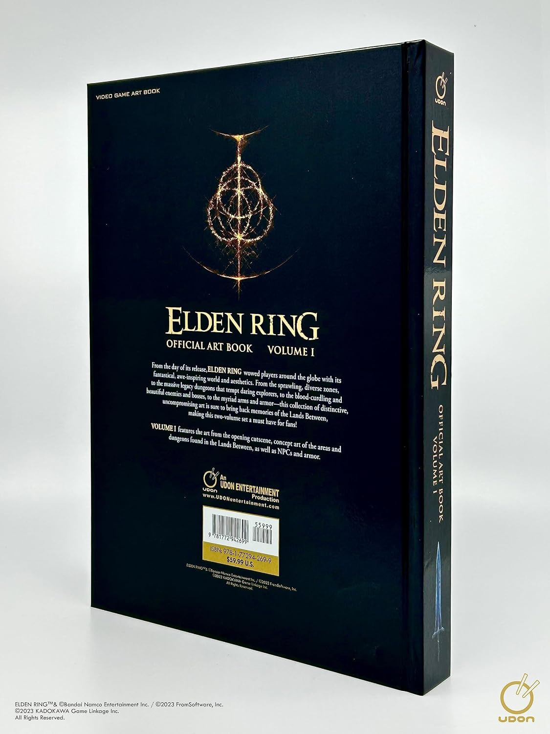 The back cover and spine of the Elden Ring Official Art Book Volume I, featuring a dark navy blue background with gold text and the Golden Compass emblem, photographed on a light gray background.
