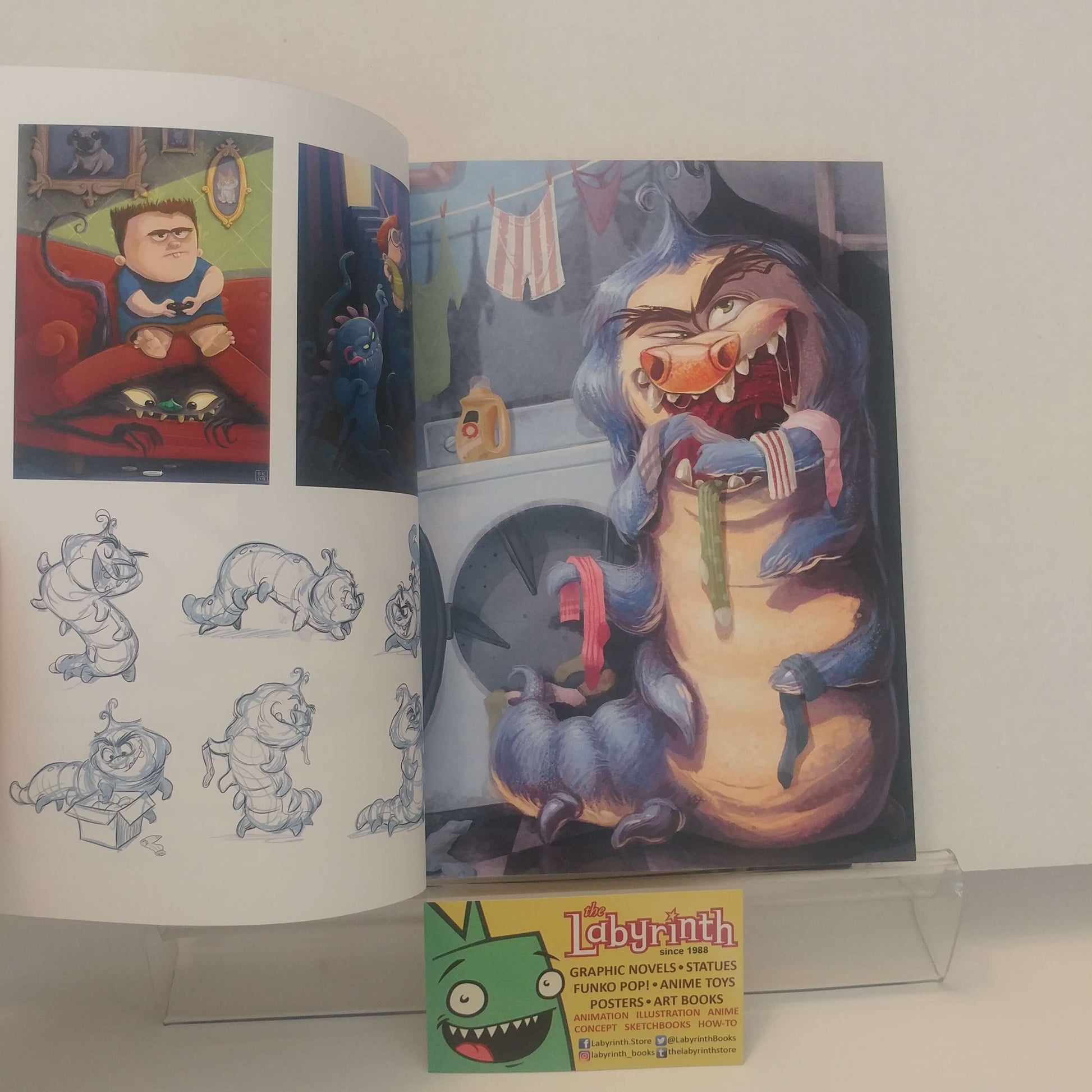 An open art book or portfolio showing illustrated pages, with a small Labyrinth trading card or insert placed in front on a clear stand against a plain light background.