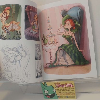 An open art print or sketchbook showing colorful illustrated scenes of a woman in a green dress and hat, alongside pencil sketches and a small Labyrinth card at the bottom.