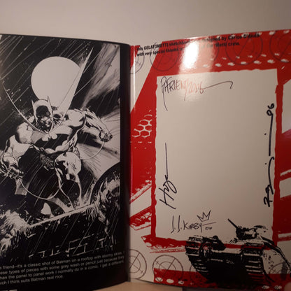An open book or printed booklet showing a black-and-white comic-style Batman illustration on the left page and a red-bordered autograph page on the right, with signatures and a tank illustration at the bottom.