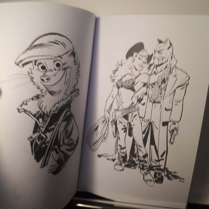 An open sketchbook or art book showing black ink illustrations on white pages. The left page has a cartoon animal portrait wearing a cap, and the right page shows a group of illustrated characters in a dynamic scene.