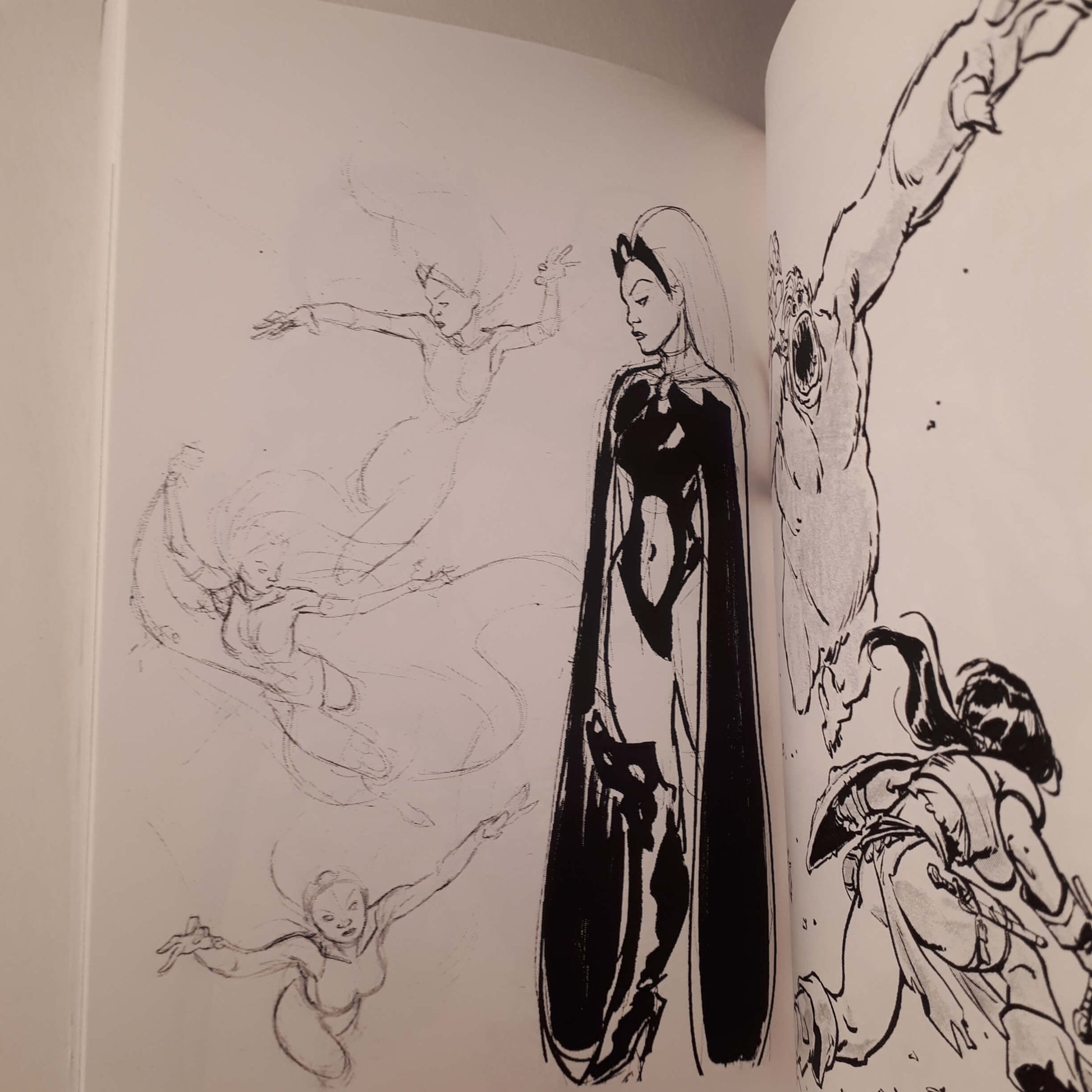 An open book or sketchbook showing black ink character illustrations on white pages, with a full-length figure in a dark dress centered on the right page and other sketchy figures around it.