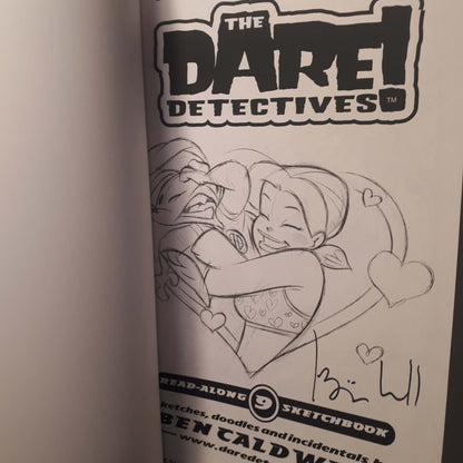 A close-up of a printed sketchbook page from 'The Dare Devoted' featuring a black-and-white line drawing of two characters hugging, with the title logo at the top and a handwritten signature near the bottom.