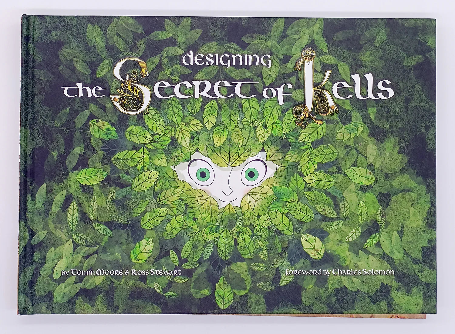 Book cover of 'Designing the Secret of Kells' with leafy design and character face.