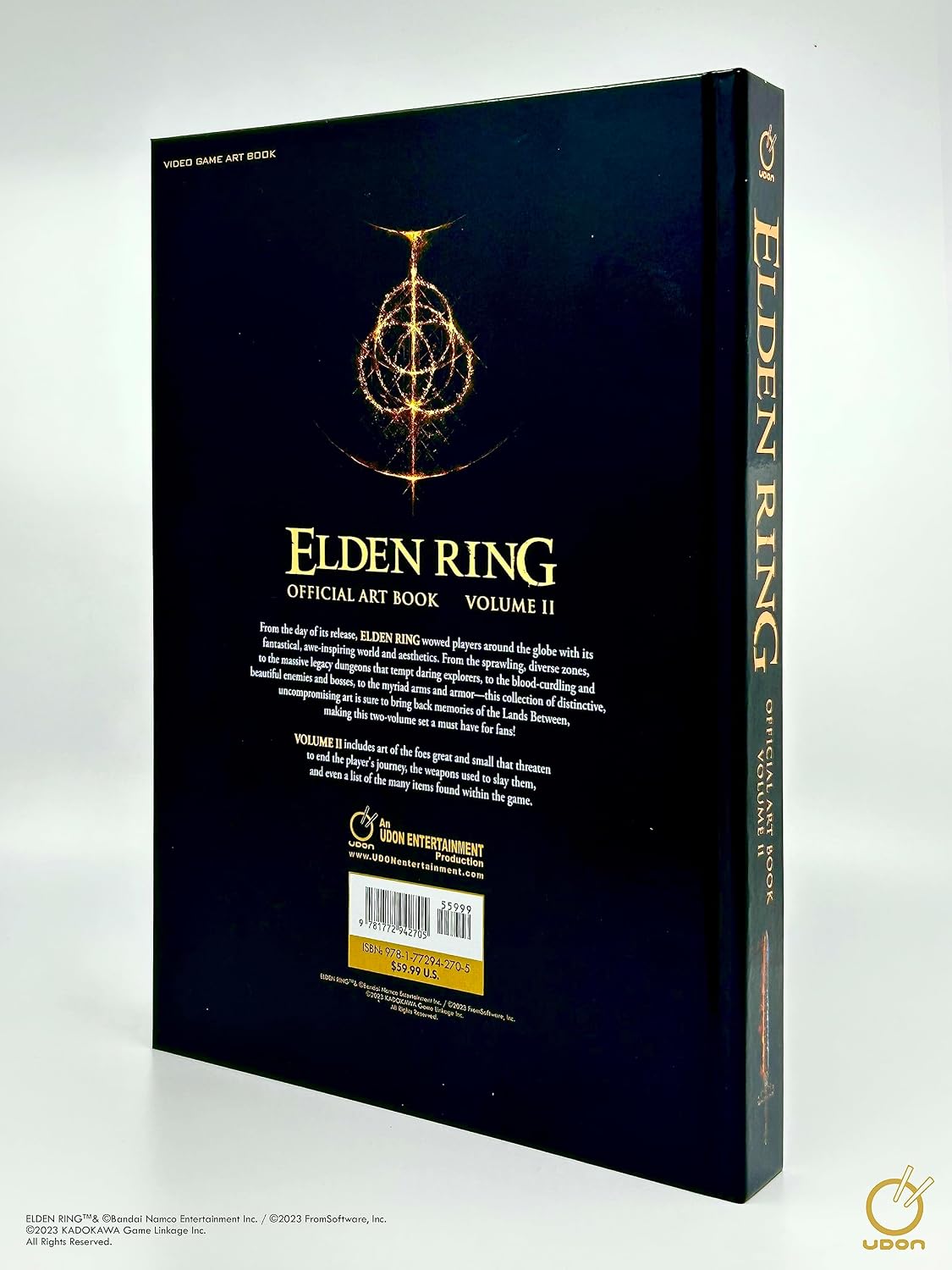 The back cover and spine of the Elden Ring Official Art Book Volume II, featuring a dark navy blue background with gold text and a glowing golden emblem, photographed on a light gray background.