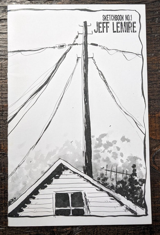A sketchbook featuring a black and white hand-drawn illustration of a house roof, power lines, and a utility pole, with the text 'SKETCHBOOK NO.1 JEFF LEMIRE' in the top right corner, placed on a dark wooden surface.