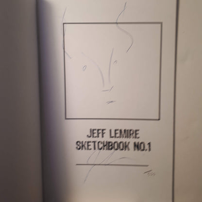 A close-up of a sketchbook page featuring a simple black line drawing inside a square frame and the text 'JEFF LEMIRE SKETCHBOOK NO.1' printed below.