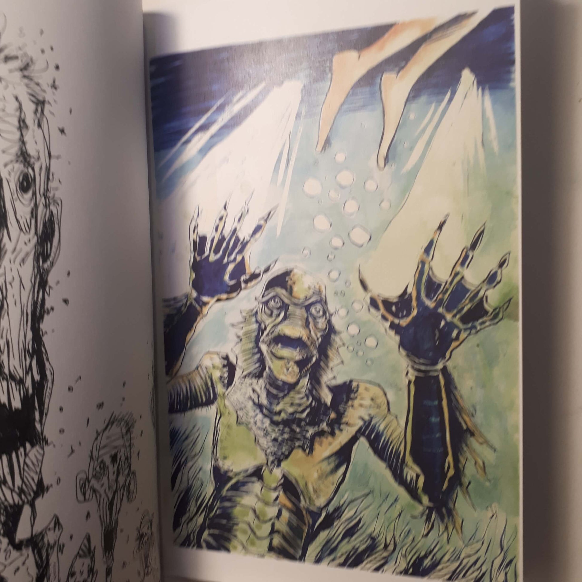 A close-up of an illustrated page showing a monstrous creature with clawed hands reaching upward in a blue-green underwater scene, with partial black line art visible on the left page.