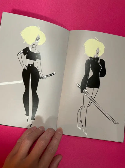 An open art book or magazine showing two stylized illustrations of a blonde woman in black outfits, one fully shaded and one outlined, held by a hand against a bright pink background.