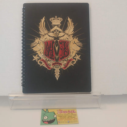 A black spiral-bound notebook featuring a large gold and red crest design on the cover, displayed on a clear acrylic stand against a white background.