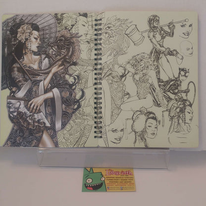 A spiral-bound sketchbook or art notebook displayed on a clear stand, featuring black line-art illustrations on cream pages. A small card with a green cartoon face and the word 'Labyrinth' is placed in front on a white surface.