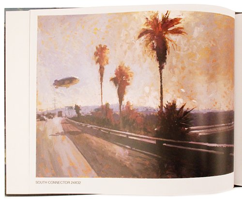 An open art book or magazine showing a painted scene of a coastal road with palm trees, a guardrail, and a small blimp in the sky. The print has a cream border with small text at the bottom reading 'SOUTH CONNECTICOR 24K32'.