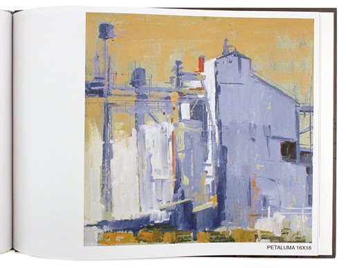 An open art book or magazine showing a painted industrial building scene. The artwork has a warm yellow sky and blue, white, and gray building forms, with the text 'PETALLUMA 16X16' printed at the bottom right of the page.