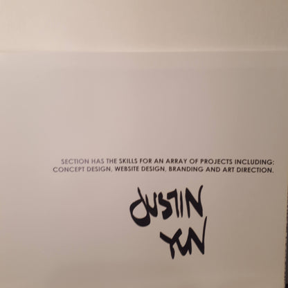 A white card or paper featuring black printed text that reads, 'SECTION HAS THE SKILLS FOR AN ARRAY OF PROJECTS INCLUDING: CONCEPT DESIGN, WEBSITE DESIGN, BRANDING AND ART DIRECTION.' Below this text is the name 'Dustin Yan' written in a stylized black script.