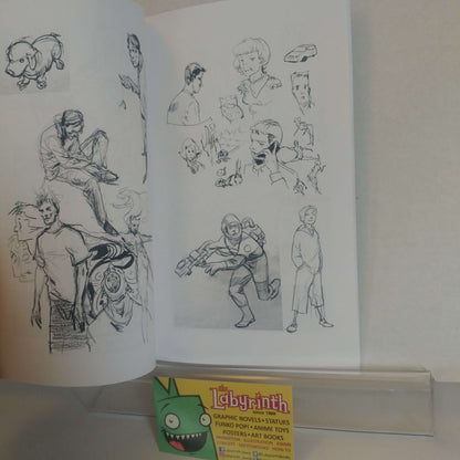 An open sketchbook displaying black ink character drawings and concept art, with a small Labyrinth branded card or box placed in front on a white surface.