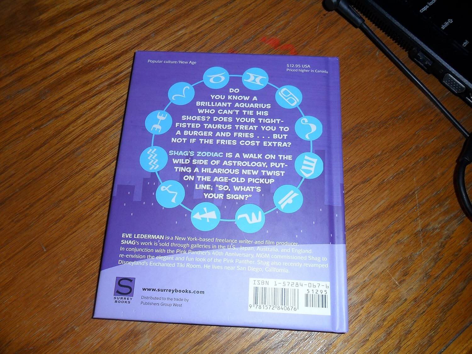 The back cover of the book 'Shag's Zodiac' by Eve Lederman, featuring a purple background with astrological symbols and text, photographed on a wooden table.