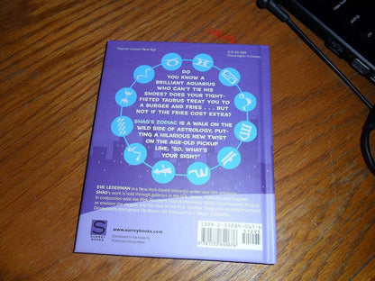 The back cover of the book 'Shag's Zodiac' by Eve Lederman, featuring a purple background with astrological symbols and text, photographed on a wooden table.