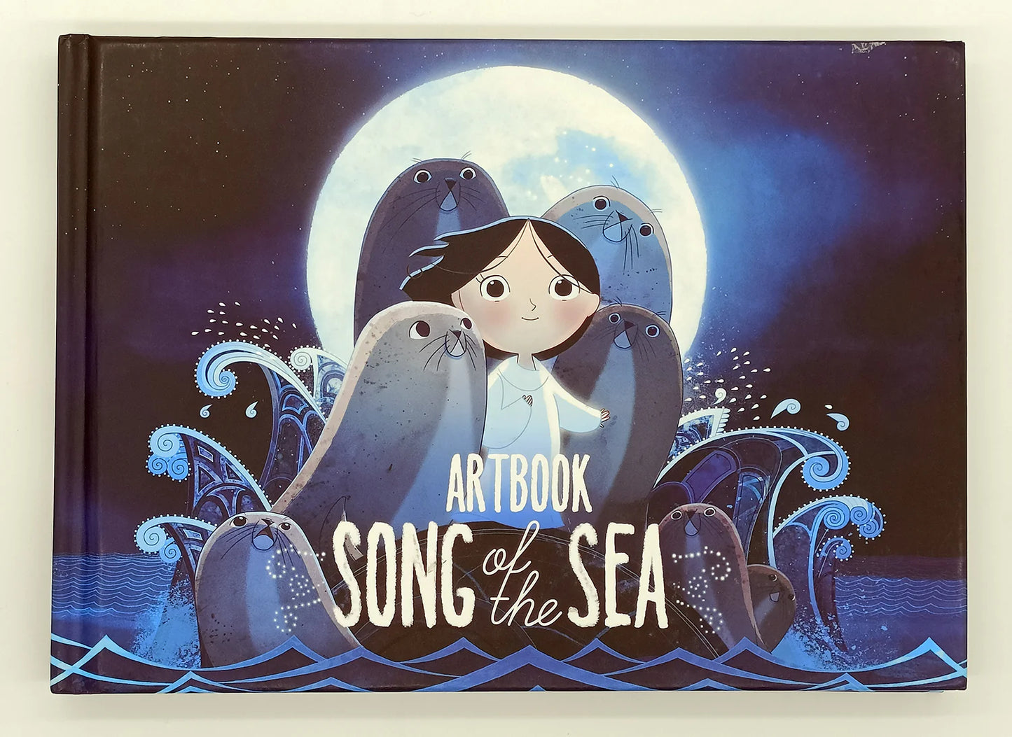 Artbook 'Song of the Sea' with illustration of a girl and seals against a moonlit sky.
