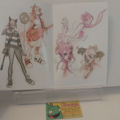 An open sketchbook displaying character concept art, with two illustrated cartoon figures and several pink-toned character studies on white pages. A small card at the bottom reads 'Labyrinth'.