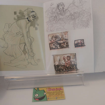 An open sketchbook or art portfolio displayed on a clear stand, showing line drawings and small painted scenes. A small card at the bottom reads 'labyrinth' and appears to be part of the presentation.