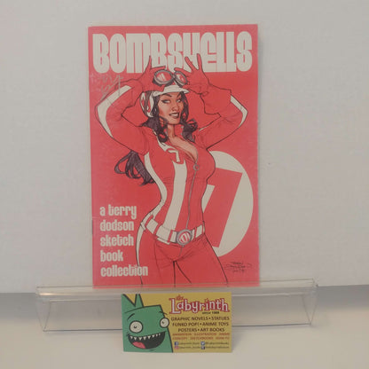 A comic book or graphic novel titled "Bombshells 7" displayed upright on a clear acrylic stand against a plain light background. The cover is predominantly pink/red with a stylized illustrated woman in a red-and-white outfit and large white title text.