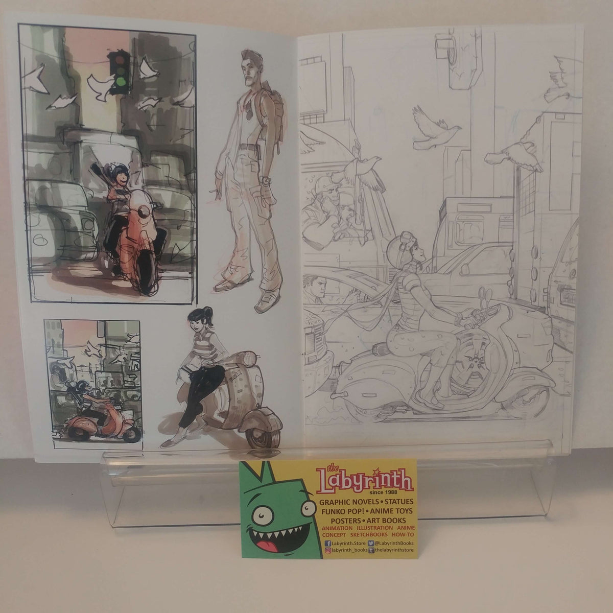 An open art book or sketchbook displayed on a clear acrylic stand, showing character illustrations and line drawings. A small card at the bottom reads 'Labyrinth' and includes a cartoon character logo.
