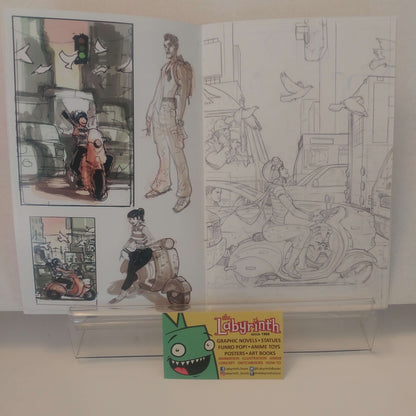 An open art book or sketchbook displayed on a clear acrylic stand, showing character illustrations and line drawings. A small card at the bottom reads 'Labyrinth' and includes a cartoon character logo.