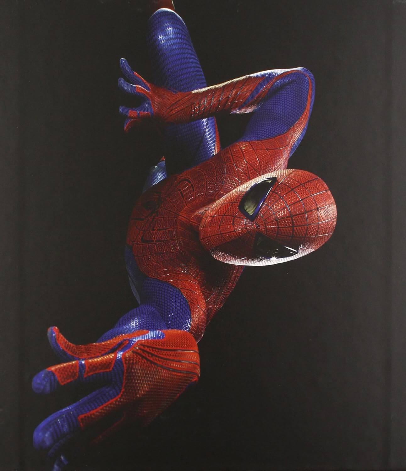 A Spider-Man figure or collectible posed hanging upside down against a dark black background, with the classic red and blue suit and web pattern clearly visible.