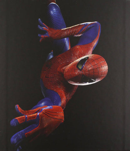 A Spider-Man figure or collectible posed hanging upside down against a dark black background, with the classic red and blue suit and web pattern clearly visible.
