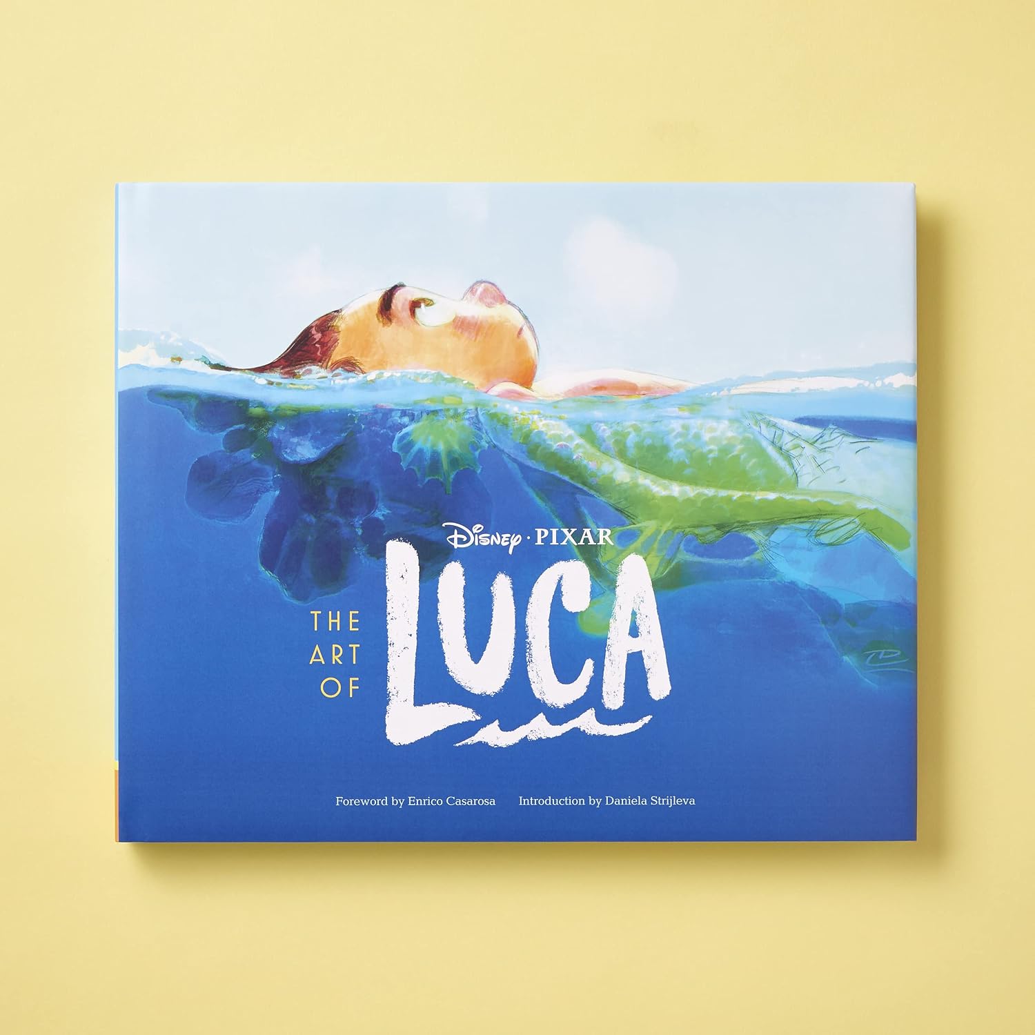 The Art of Luca book cover by Disney Pixar, featuring a split water illustration with a character floating at the surface, set against a solid pale yellow background.