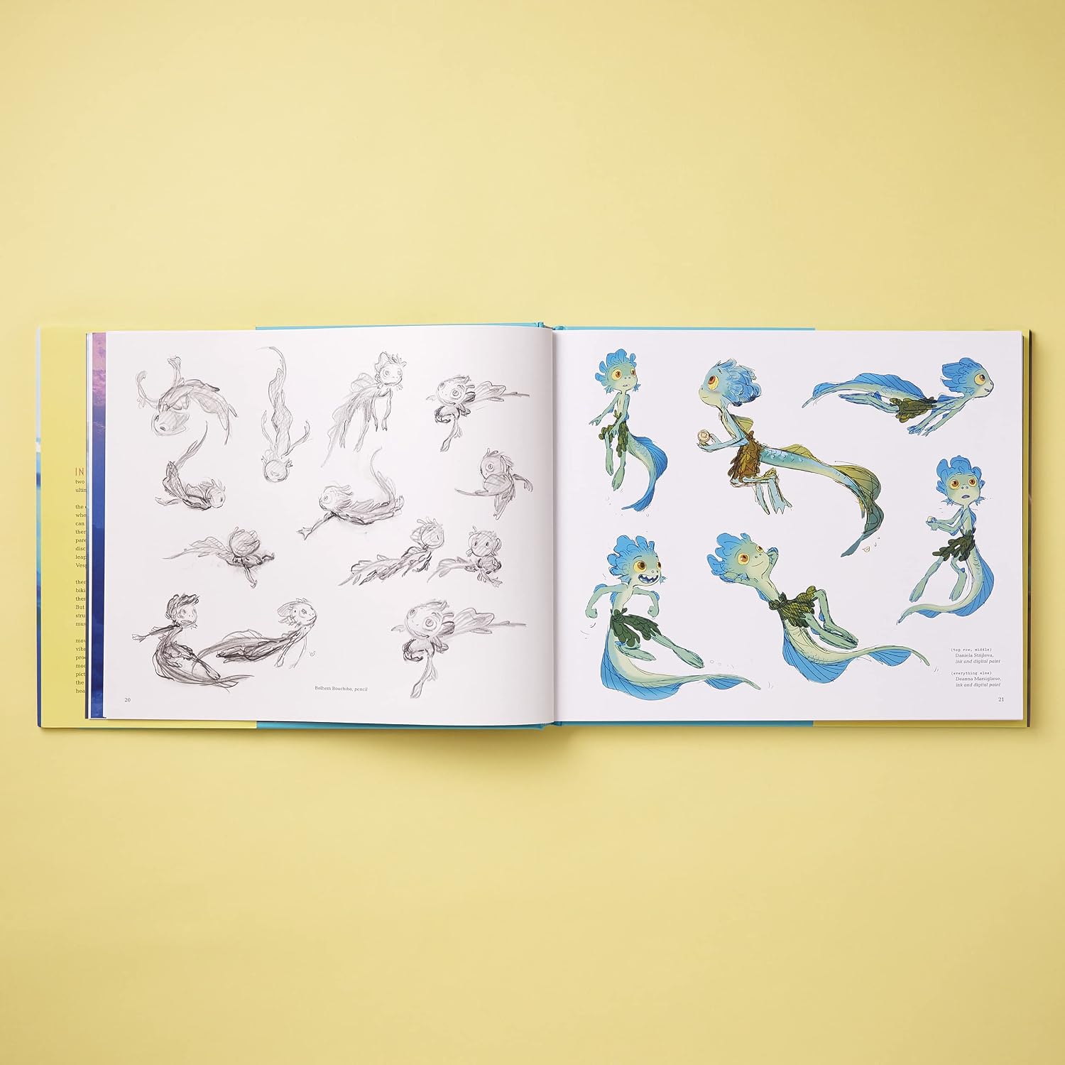An open art book or concept sketchbook laid flat on a pale yellow background, showing character designs and pencil studies on both pages. The illustrations feature blue, green, and brown fantasy figures on white paper.