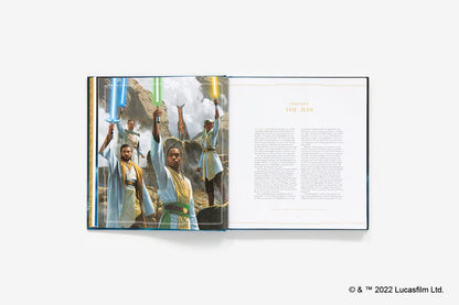 An open hardcover book displayed on a light gray background, showing a printed cover illustration with figures holding lightsabers on the left page and text columns on the right page. Small Lucasfilm Ltd.