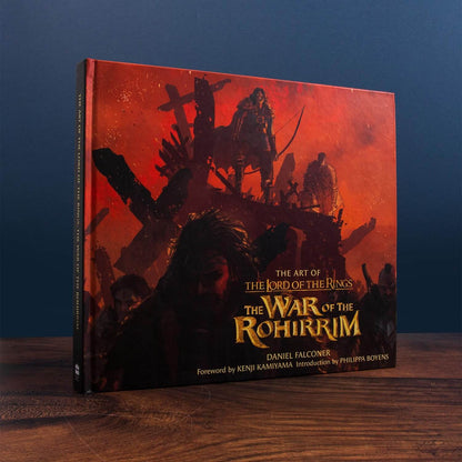 Book titled 'The Art of The Lord of the Rings: The War of the Rohirrim' on a wooden surface with a dark blue background
