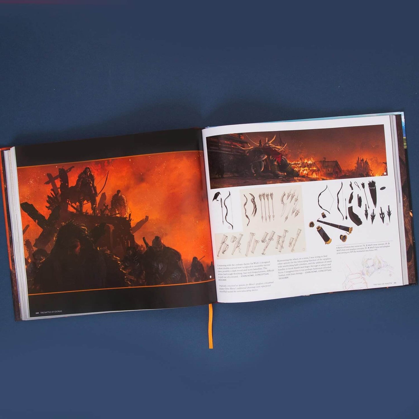 An open art book or magazine laid flat on a dark blue background, showing two printed pages with fiery orange and black fantasy artwork and a small sheet of illustrated weapon-like designs.