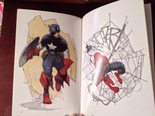An open illustrated book or art print showing comic-style superhero artwork: Captain America on the left page and Spider-Man on the right page, photographed against a dark wooden surface.